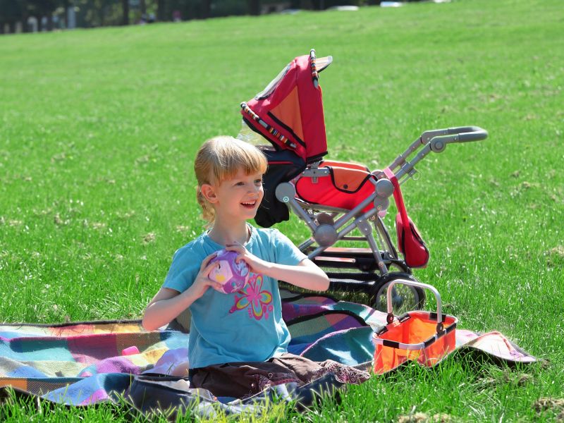 Ein Kind sitzt auf einer Picknickdecke in der Sonne und spielt.